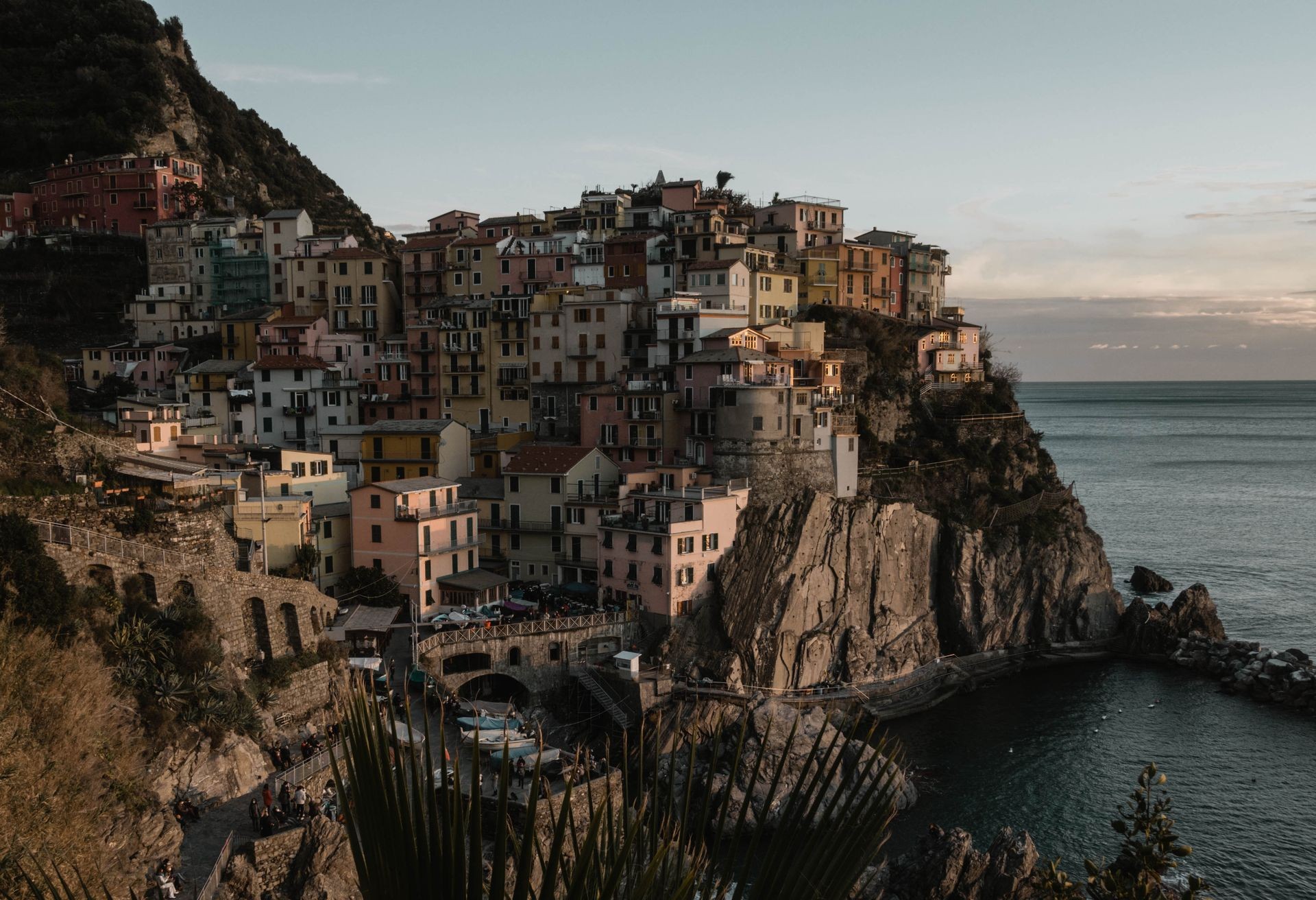 Colorful buildings perched on a rocky cliff by the sea at sunset.