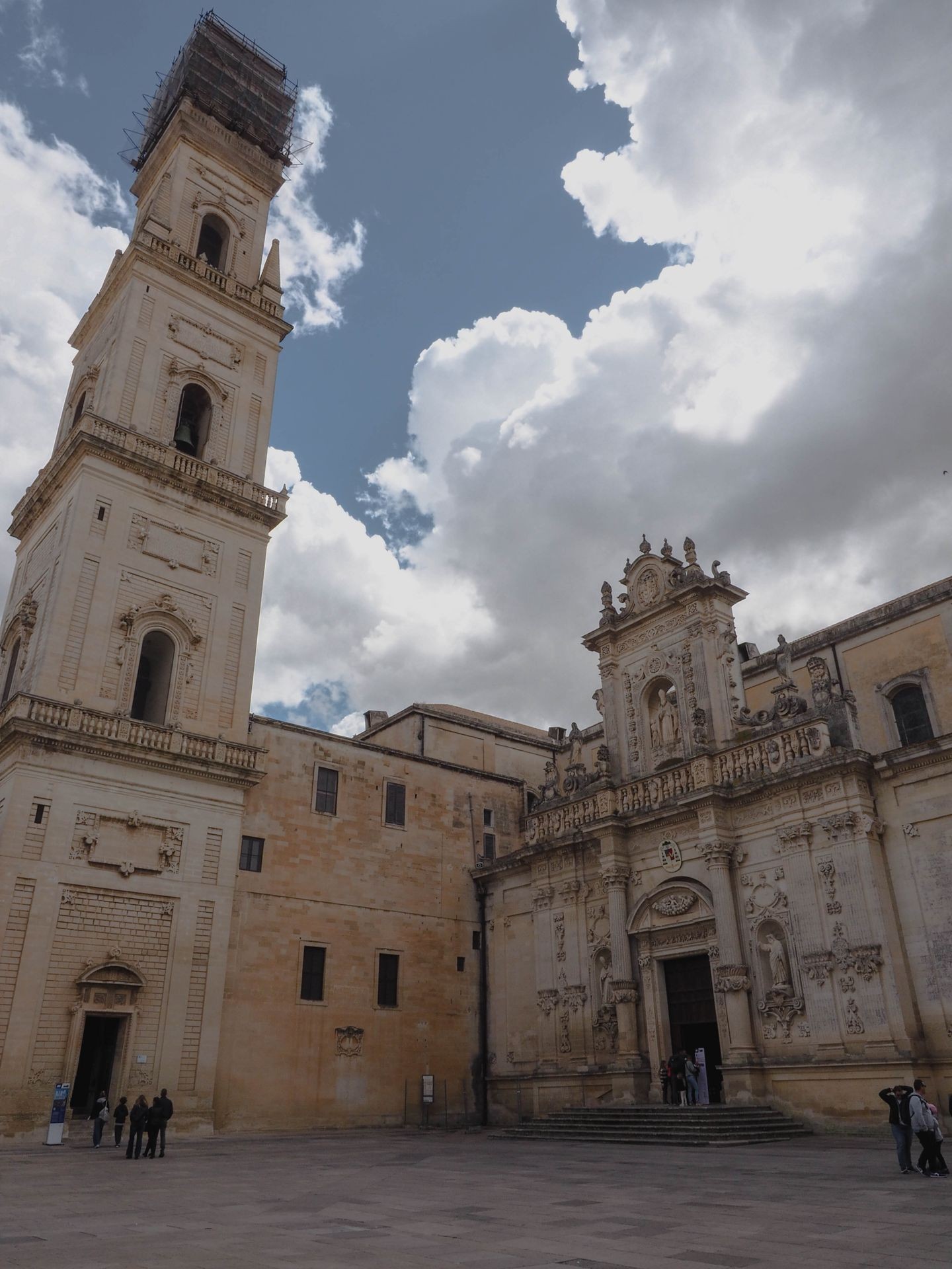Historic church with ornate facade and tall bell tower against a cloudy sky, people gathered near entrance.