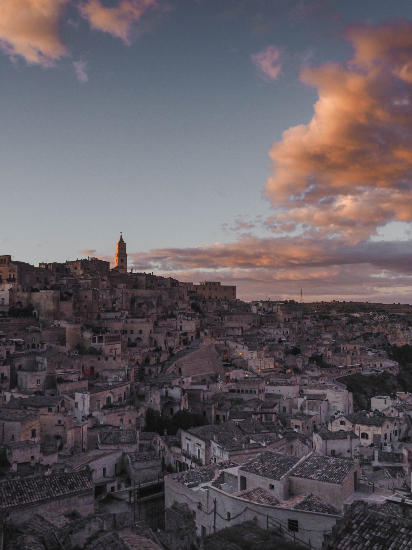 Ancient hillside town at sunset with dramatic clouds and a prominent clock tower.