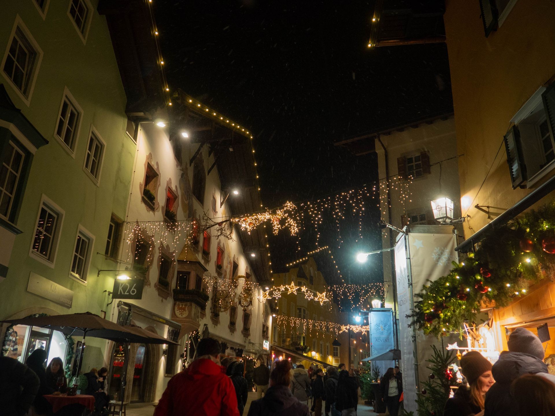 Christmas market street view at night with festive lights and decorated buildings, crowded with people.